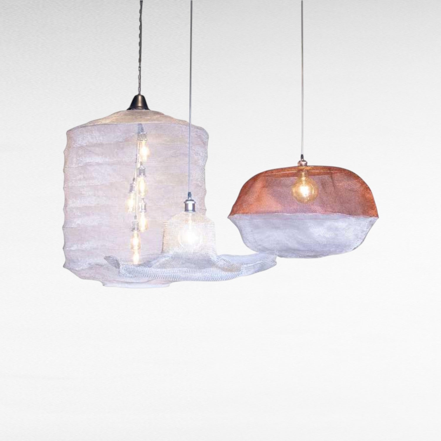 Chora Barefoot Luxury Living handwoven metal wire pendant lights in cloud shapes, one copper and white, one white with multiple bulbs.
