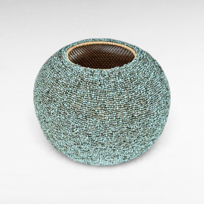 Chora Barefoot Luxury Living light blue and green beaded rattan basket with a textured, round decorative design.