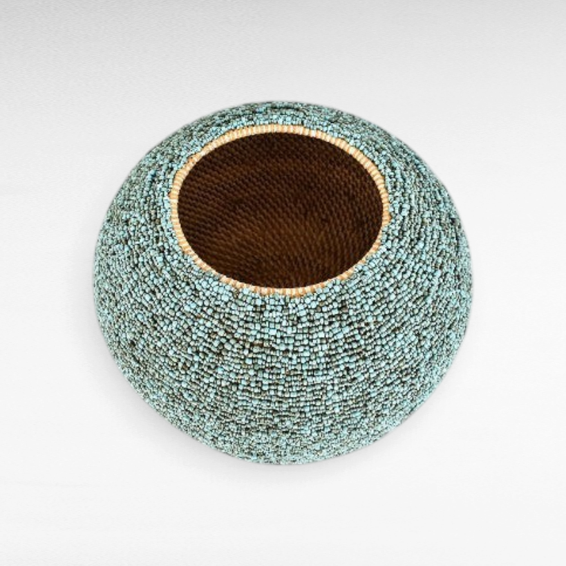 Chora Barefoot Luxury Living round rattan basket with light blue and green beaded texture on a white background