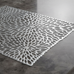 Chora Barefoot Luxury Living silver non-woven fabric placemat with intricate floral cut-out pattern on grey table