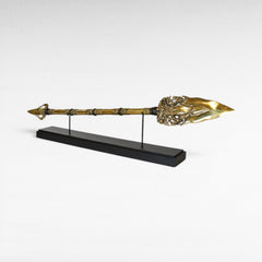 Chora Barefoot Luxury Living ornate brass golden spear with decorative detailing and a black display stand.