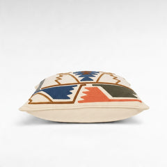 Chora Barefoot Luxury Living cream square pillow with geometric embroidery in blue, brown, orange, and olive green.