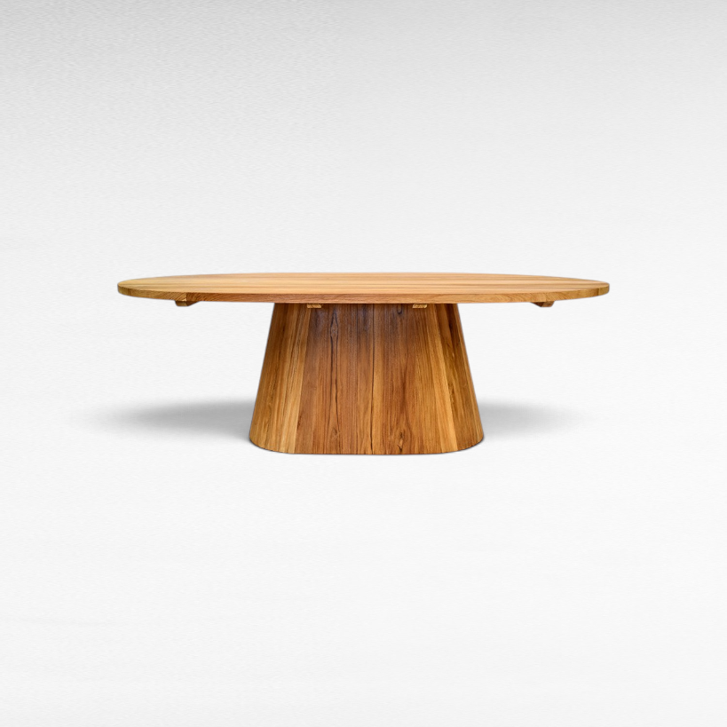 Chora Barefoot Luxury Living oval suar wood dining table with a solid pedestal base and natural honey grain patterns.