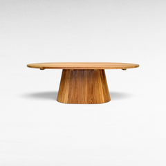 Chora Barefoot Luxury Living oval suar wood dining table with a solid pedestal base and natural honey grain patterns.
