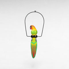 Chora Barefoot Luxury Living colorful wooden parrot decoration with yellow, green, and orange accents hanging from a black metal stand.
