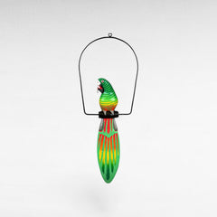 Chora Barefoot Luxury Living green and red painted wooden parrot decoration with yellow accents, hanging from a black metal frame.