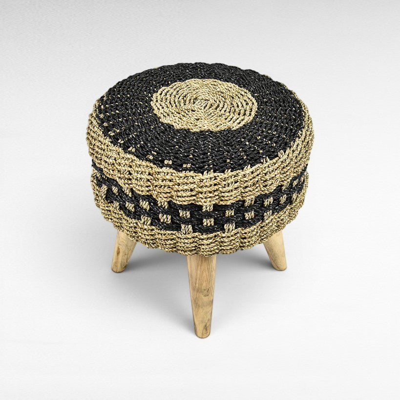 Chora Barefoot Luxury Living round stool with a black and natural hand-braided synthetic rattan seat and teak wood legs.