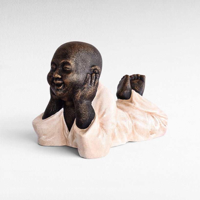 Chora Barefoot Luxury Living Figurine Shaolin, a fiber cement statue of a monk resting on its stomach with hands on cheeks.