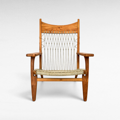 Chora Barefoot Luxury Living teak wood armchair with a woven synthetic raffia seat and decorative knotted backrest.