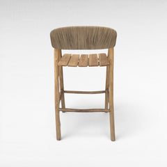 Chora Barefoot Luxury Living teak wood bar stool with synthetic raffia seat and slatted wood footrest.