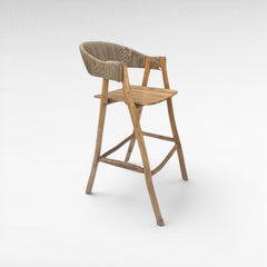 Chora Barefoot Luxury Living teak wood bar stool with woven synthetic raffia seat and back, natural wood finish.