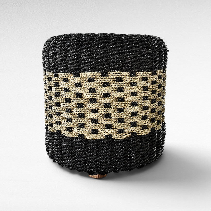 Chora Barefoot Luxury Living cylindrical stool made of woven black and natural grass rope with a textured pattern.