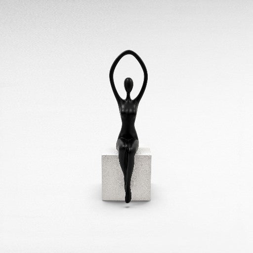 Chora Barefoot Luxury Living black abstract female figurine with arms raised, seated on a white textured cube stand.