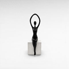 Chora Barefoot Luxury Living black abstract female figurine with arms raised, seated on a white textured cube stand.