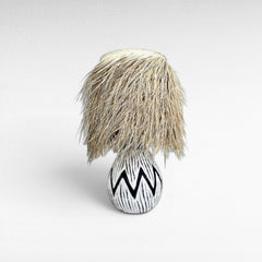 Chora Barefoot Luxury Living black and white zigzag patterned ceramic table lamp with a natural raffia fringe shade.