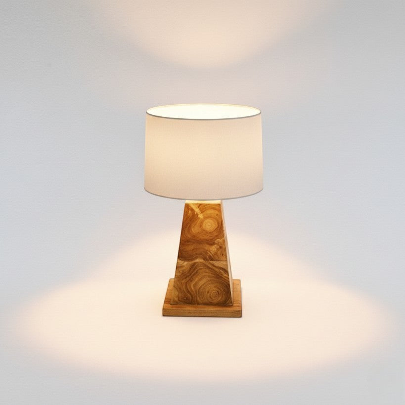 Chora Barefoot Luxury Living natural teak wood table lamp with unique grain patterns and a white drum shade, providing ambient light.